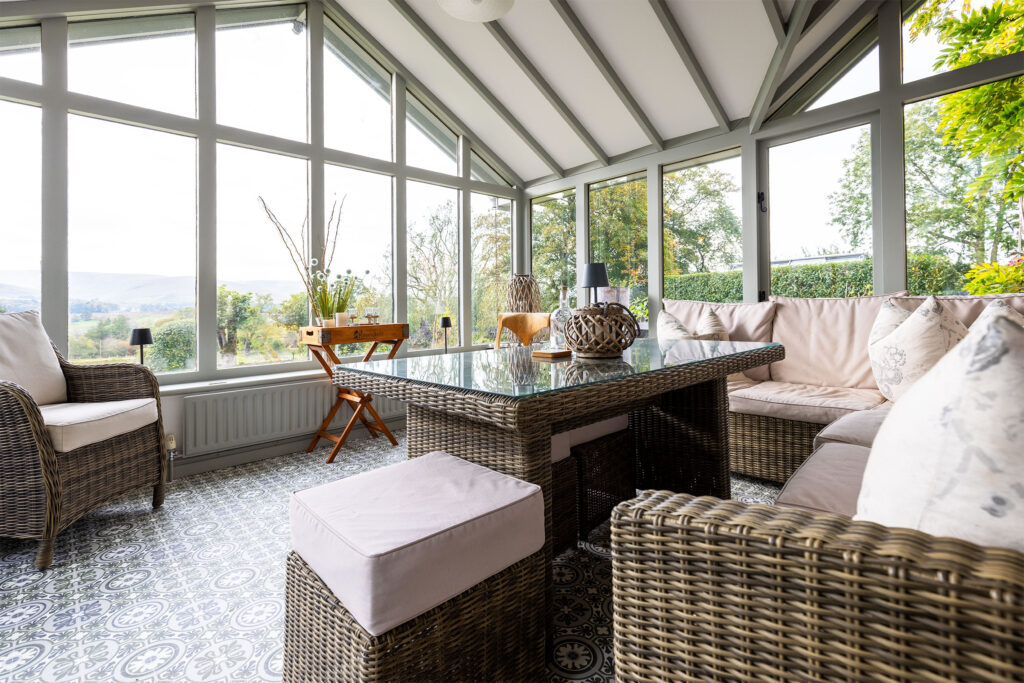 Bright conservatory with large windows, wicker furniture, and countryside views, captured using commercial photography for property and interior marketing.