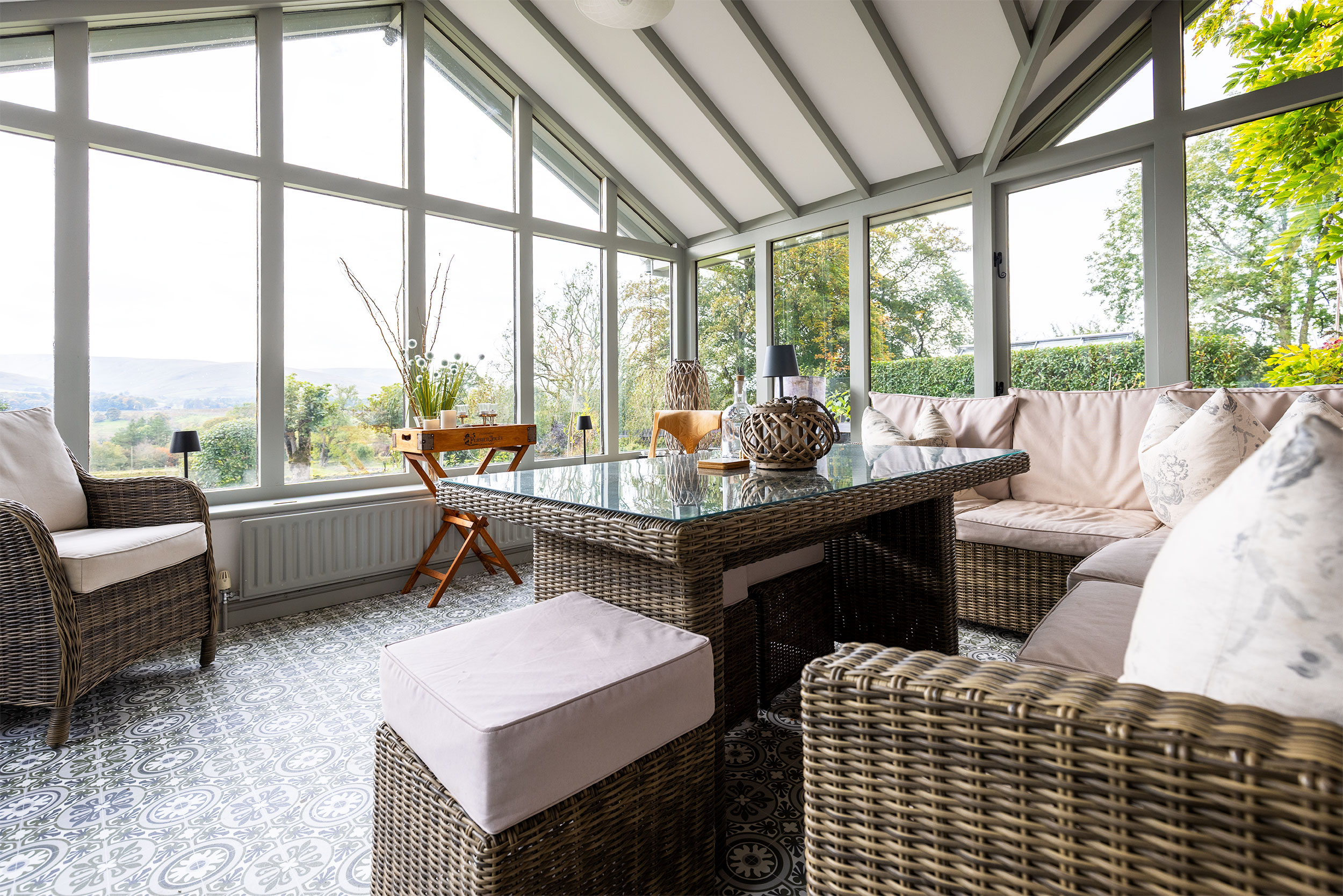 Bright conservatory with large windows, wicker furniture, and countryside views, captured using commercial photography for property and interior marketing.