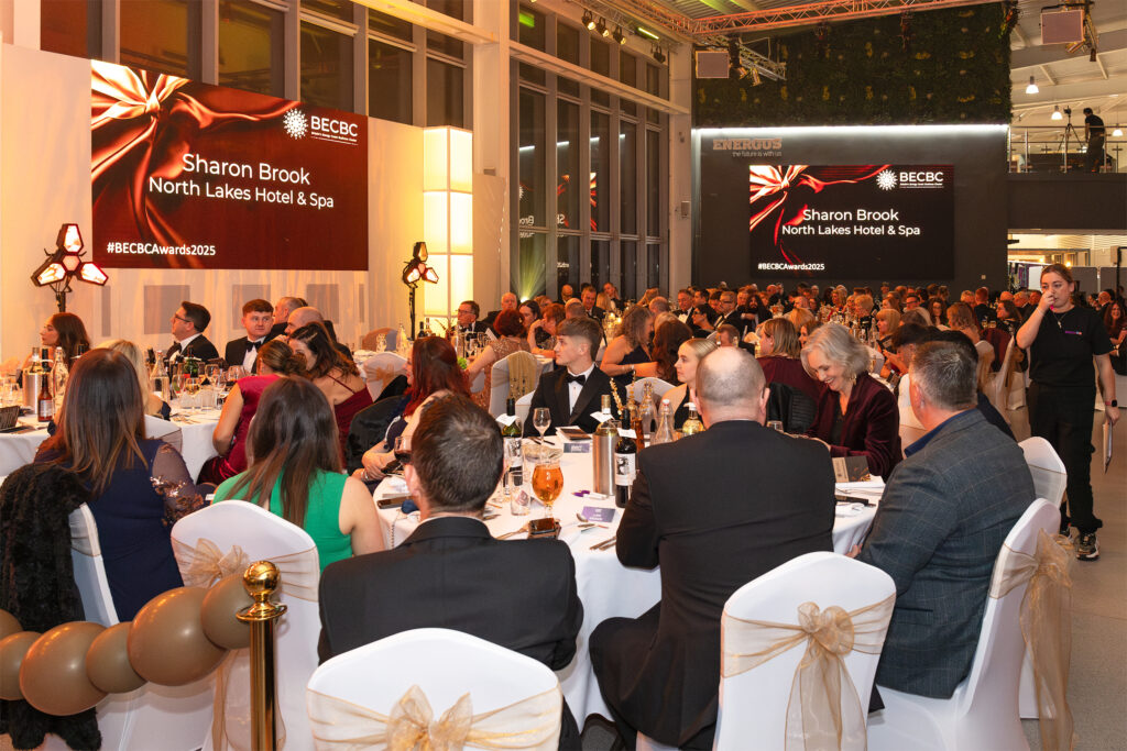A large formal awards event with guests seated at decorated tables, watching a presentation screen displaying BECBC Awards 2025 in a modern venue.