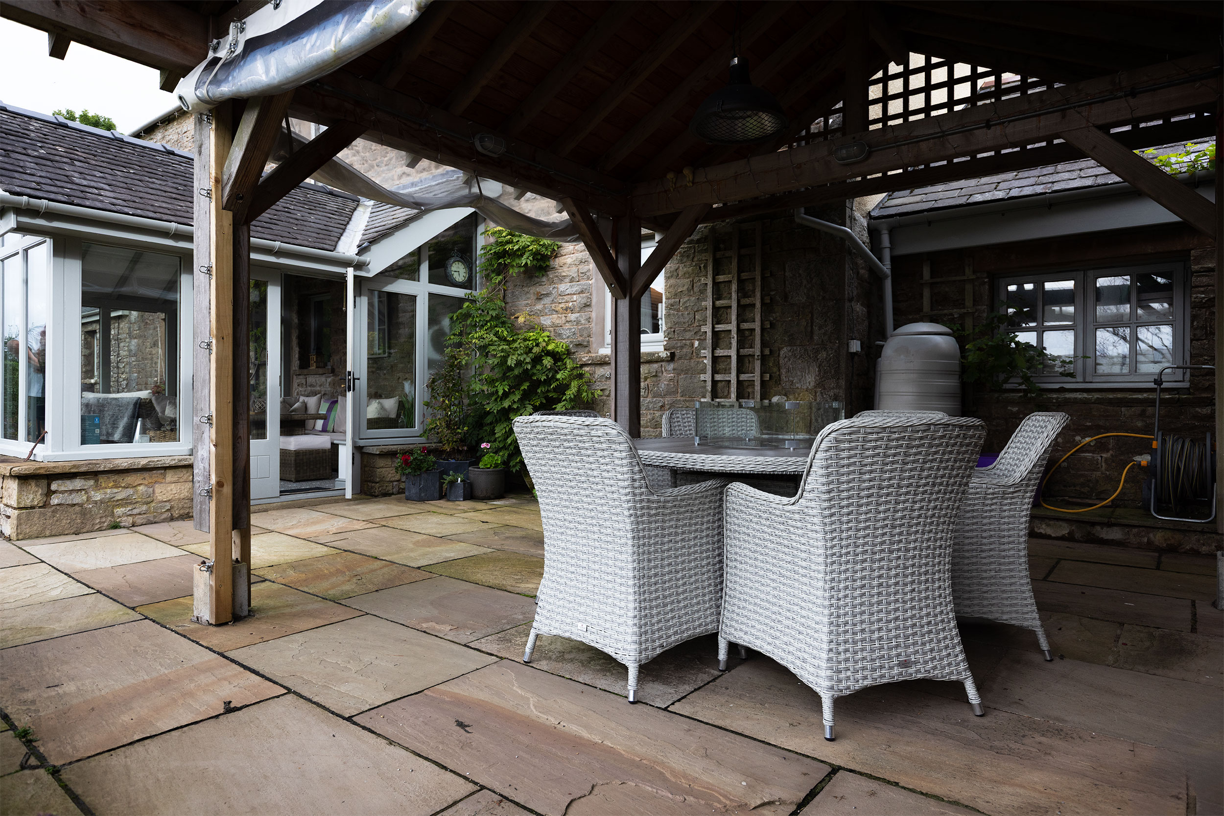 Outdoor patio with covered seating area, wicker dining furniture, and stone-built property, captured using commercial photography for hospitality and property marketing.
