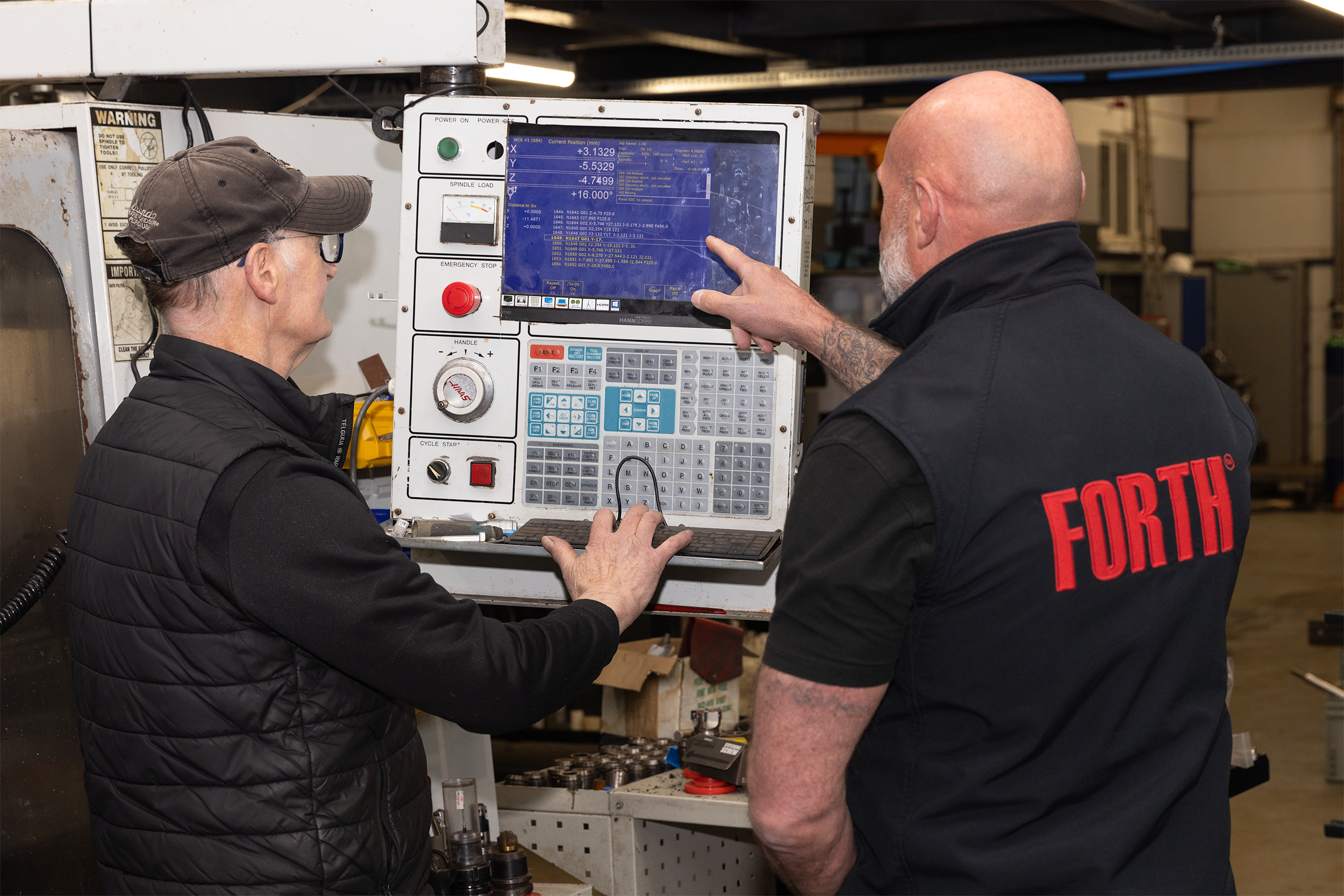 Industrial photographer in Cumbria capturing two engineers operating a CNC machine in a busy workshop at Forth Engineering, highlighting precision machining and teamwork